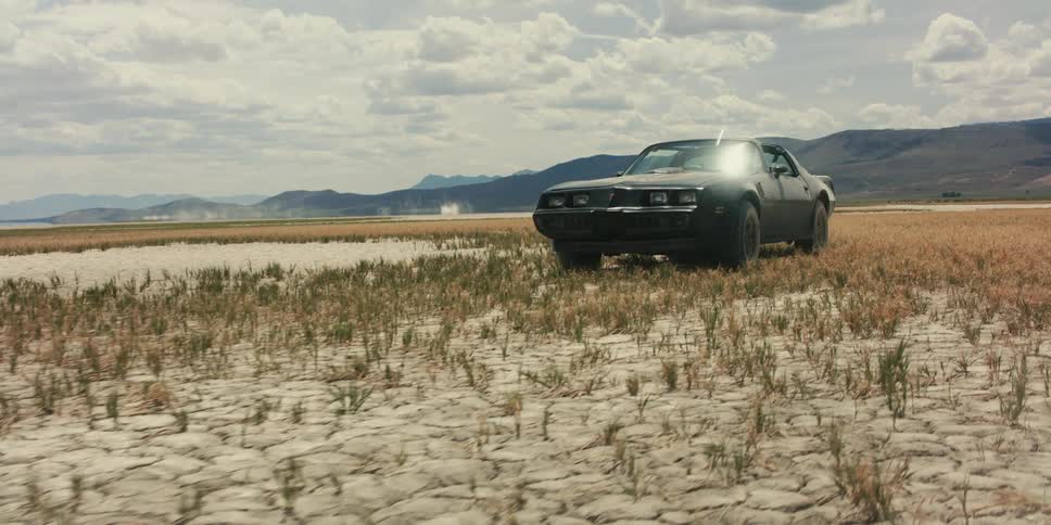 Black muscle car parked on the desert near the mountain moves forward kicking dust