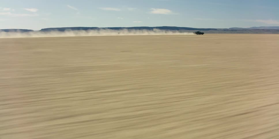 Black performance car drives fast and raising dust trail across the desert