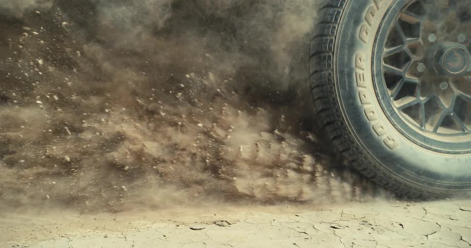 A goodyear cobra tire kicks up dirt and sand leaving a cloud behind