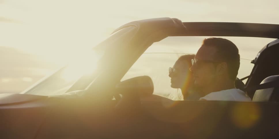 Couple drive along on sunny day with top down