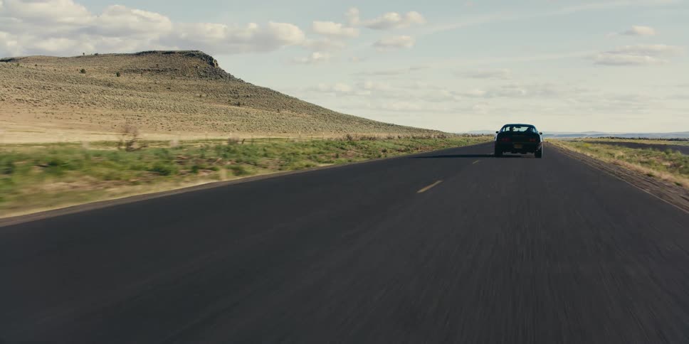 Black car driving on a road through the desert at morning