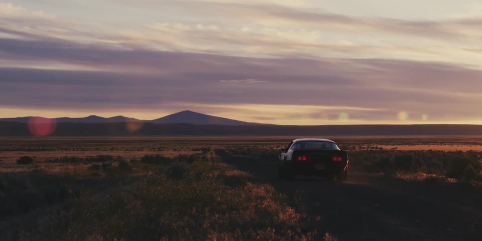 A sports car is traveling on a desert road with mountains in the distance