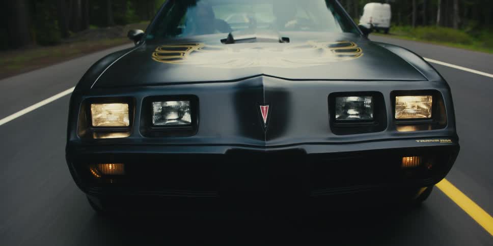 Black sports car with eagle decall with headlights on driving on a rural road