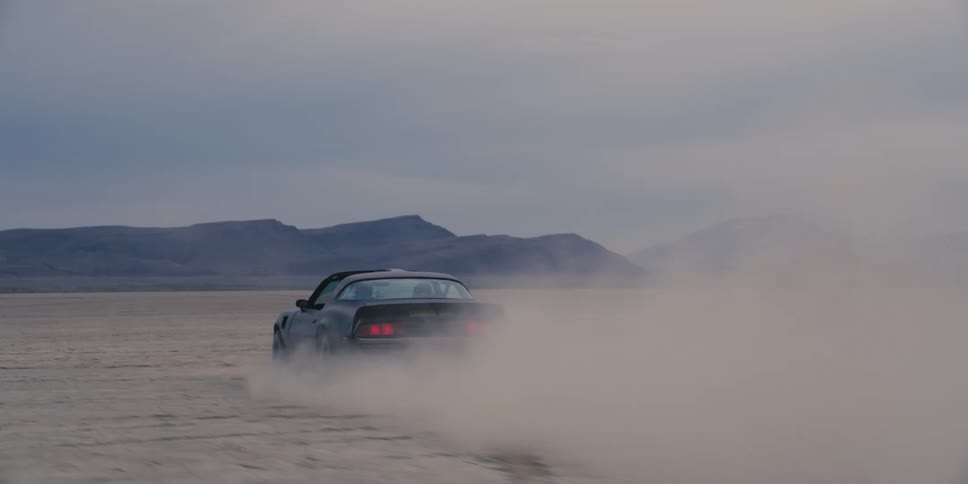 Black muscle car kicks dust while driving on the desert near the mountains
