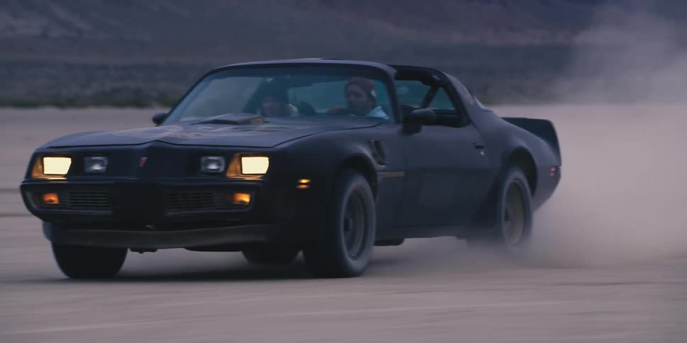 Young couple driving a fast black muscle car on the desert at evening