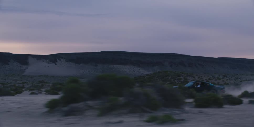 Black muscle car driving on the badlands near the mountains at sunset