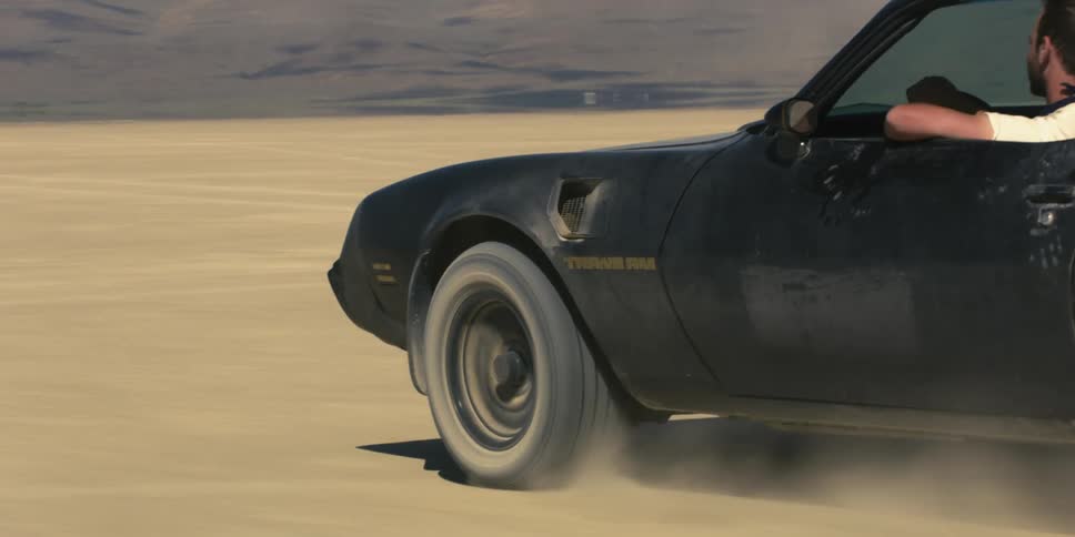 A black trans am travels on a desert road