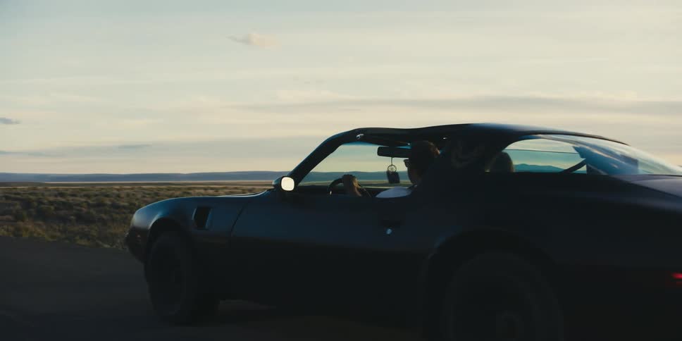 Two people are traveling on a lonely highway in a sports car in a desert region in the evening