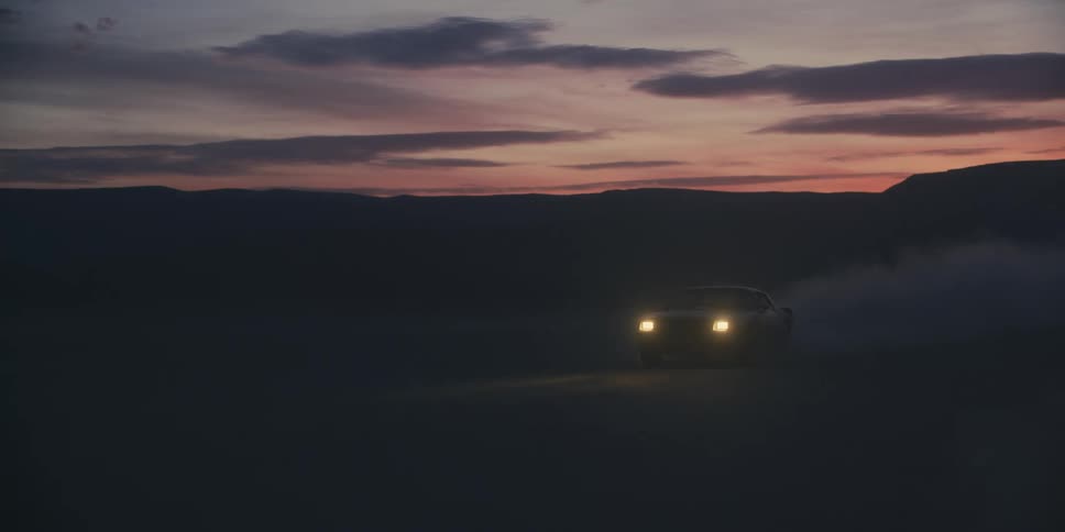 Car speeds across desert at night under red sky kicking up dust