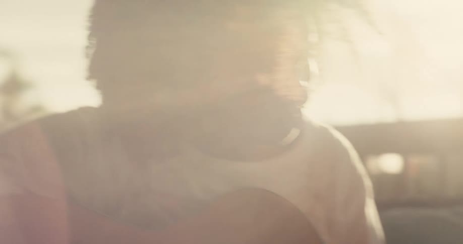 A black person sitting outdoors playing a guitar