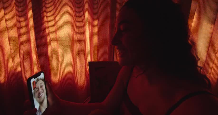 Young woman inside a room with a red curtain talking with a man on a video call