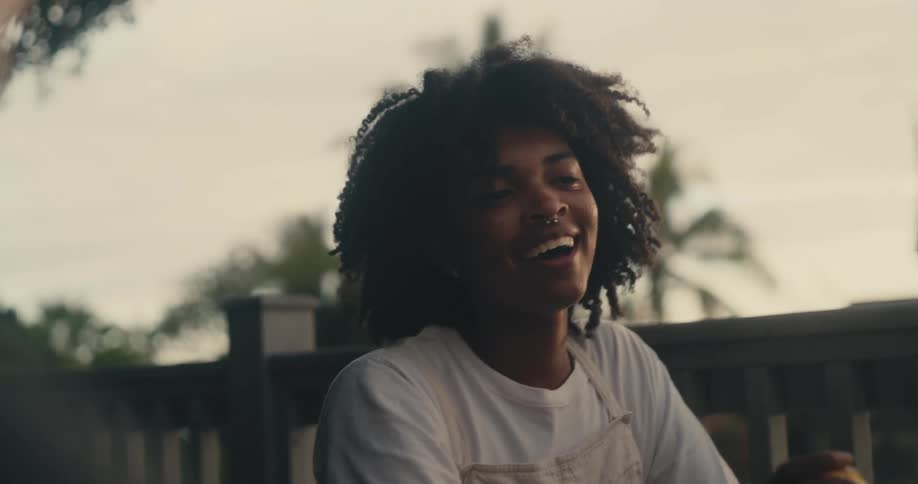 Woman with curly hair nose piercing white shirt and apron drinks beverage smiling at man
