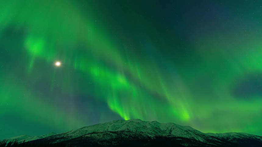 Waves of green light dance in the sky above a snow capped ridge