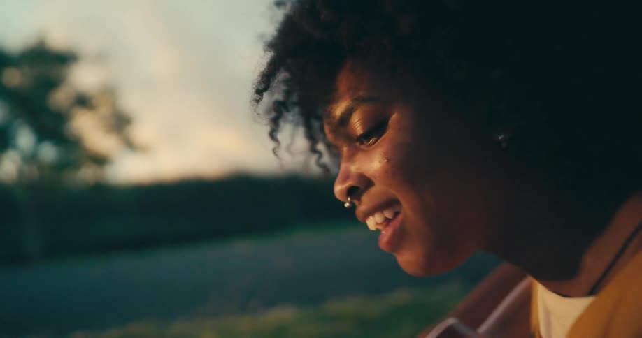 A woman sitting on grass playing a guitar with the sky and clouds in the background