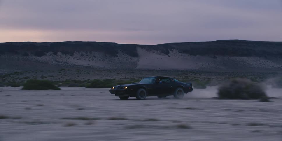 A man drives a vintage car around brush in the desert
