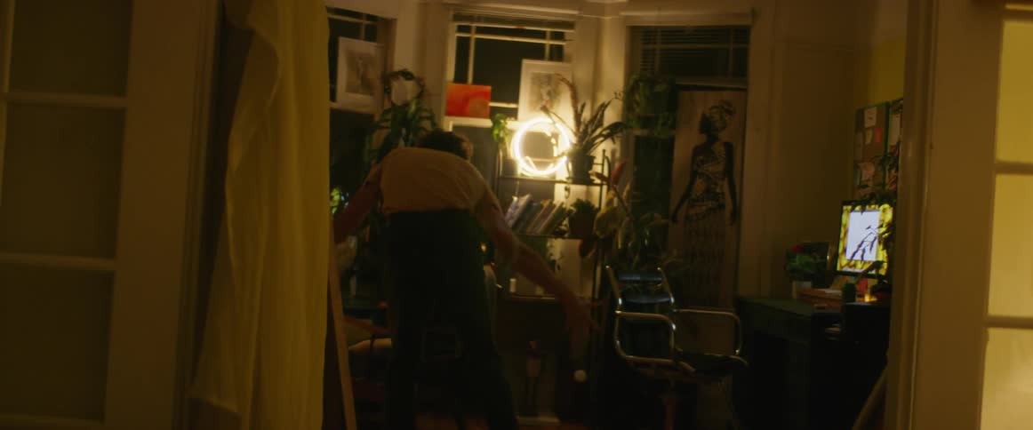 Man with yellow shirt black pants dances next to desktop in dim lit room