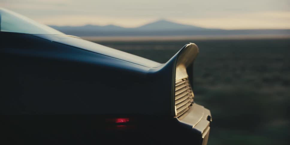 Black sports car driving on a rural road near the mountains at sunset