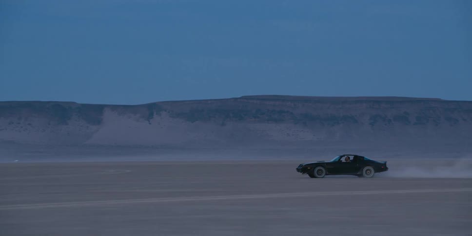 Black performance car drives fast and raising dust trail across the desert