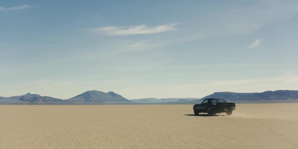 Black muscle car kicking dust on a desert near the mountains