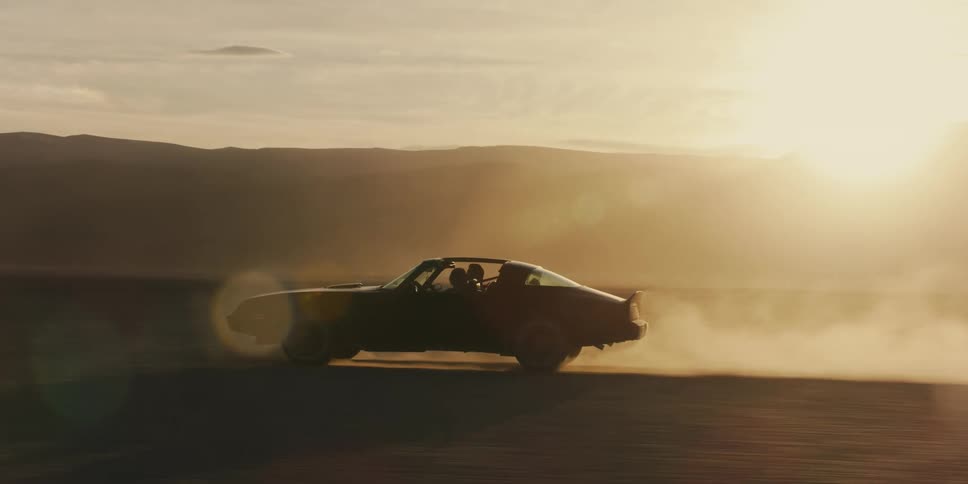 Black muscle car kicking dust driving on the desert near the mountains at sunset