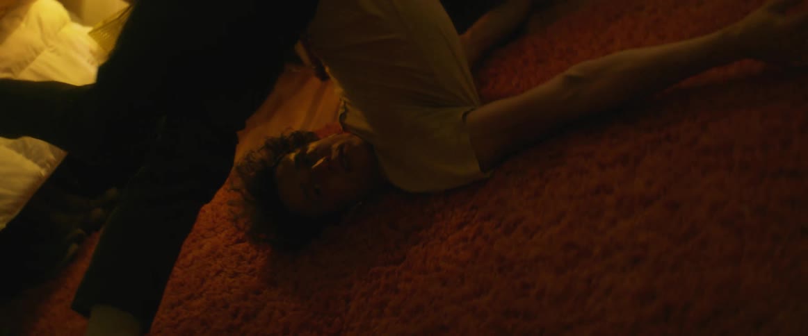 A teenage boy with ear bugs in rolls around on a carpet at home and lifts his body up and down