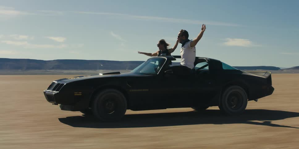 Young couple sitting out the window of a moving car in the desert