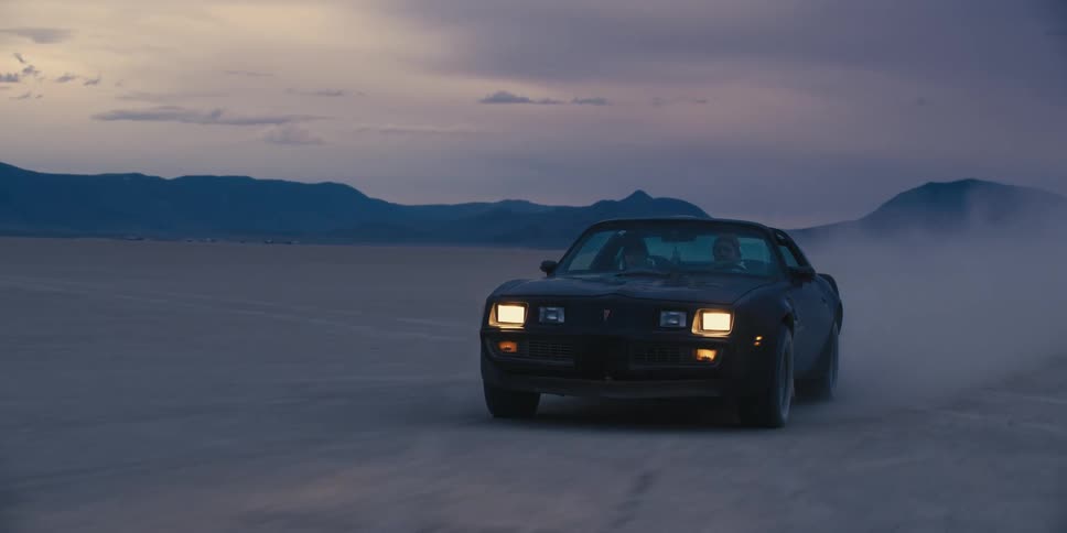 Black sports muscle car kicking up dust driving on a desert near the mountains at sunset