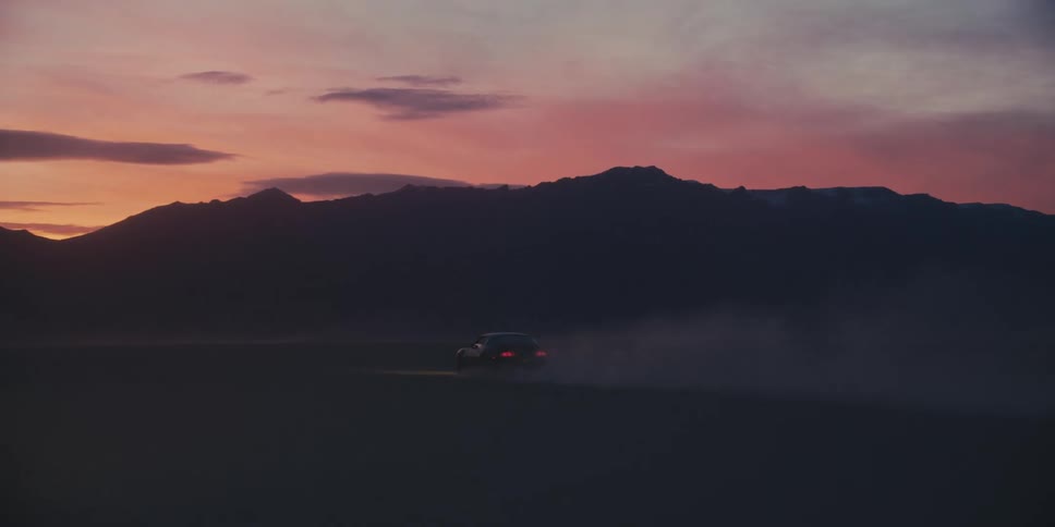 Black muscle car kicking dust while driving on the desert near the mountains at sunset