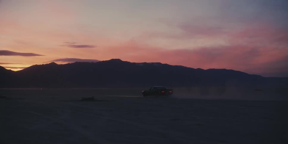 Car drives in the field with distant mountainand red sky in the background