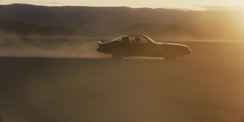 Performance car drives with dust trail in desert at sunset