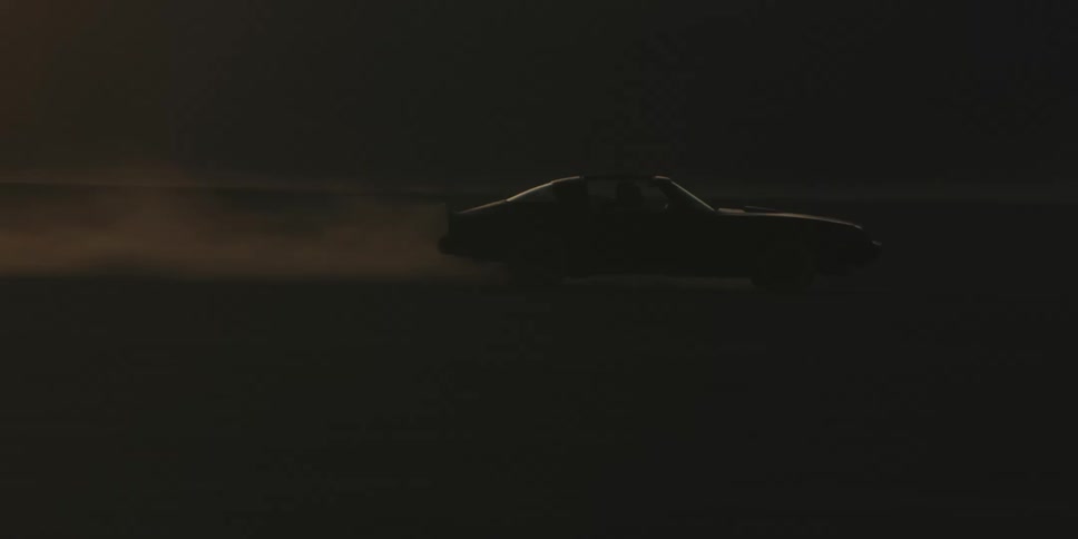 A car driving on a desert with a mountain range the sky and clouds in the background