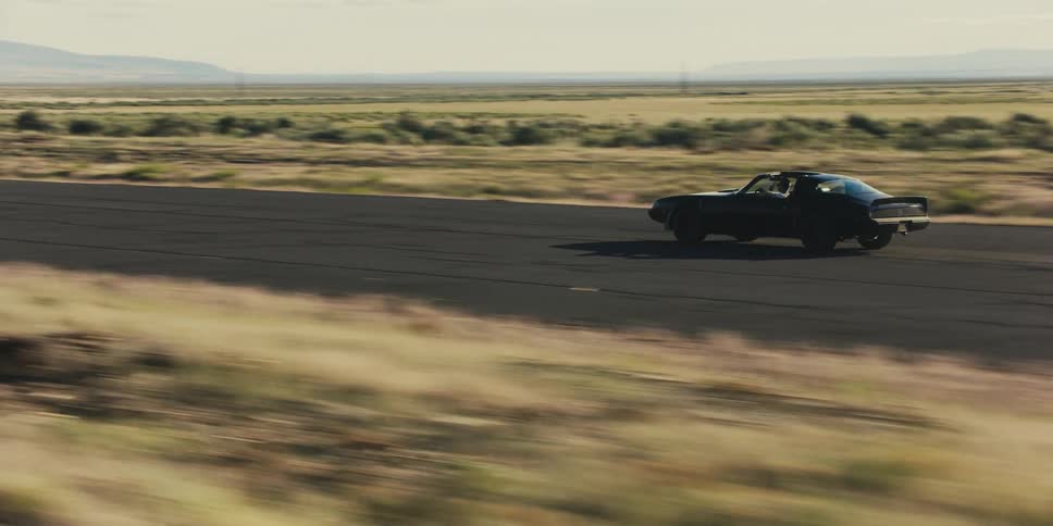 A sports car with a t roof travels on an empty desert road