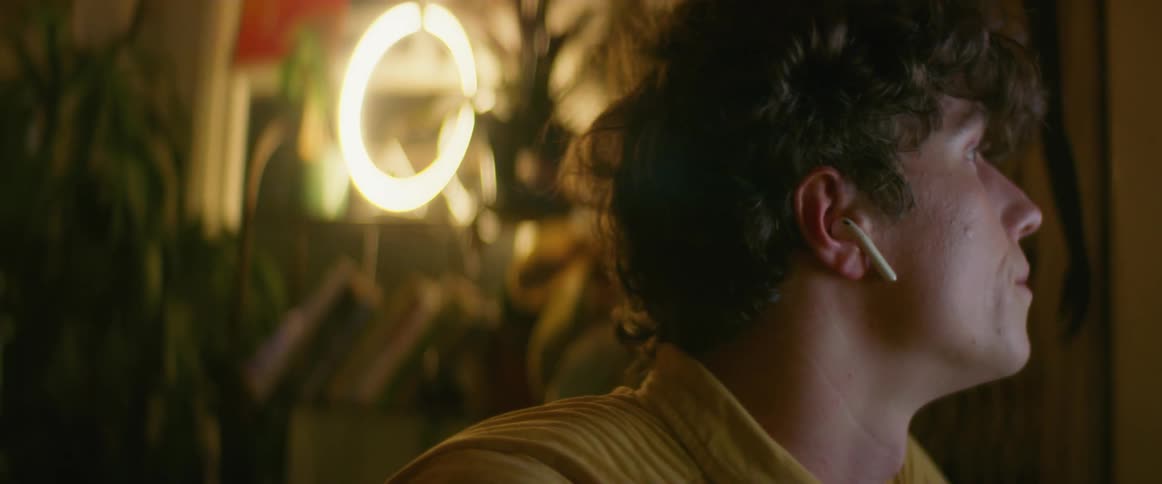 Side view of man with curly hair and earphones looking at computer screen in dim lit room
