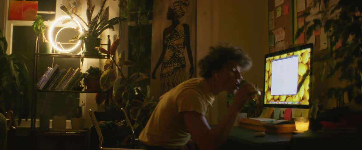 A male in a living room drinking and sitting in front of a computer