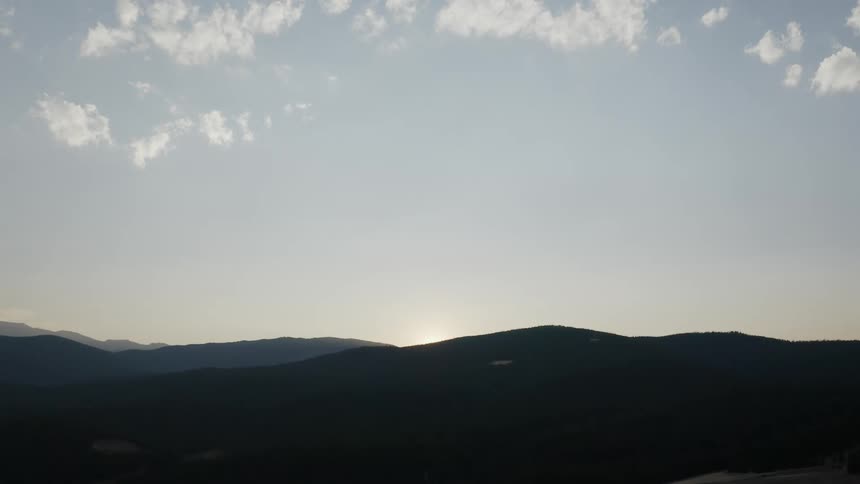 A wide shot of a mountain range just as the sun sets out of view