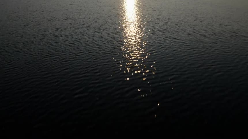 A body of water with land the sun the sky and clouds in the background