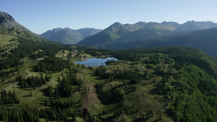 Aerial view of hills with trees overlooking small lake and distant mountain range