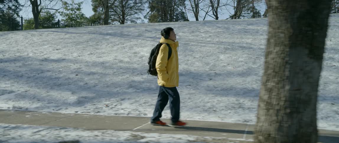 A boy is walking along the sidewalk near a hill