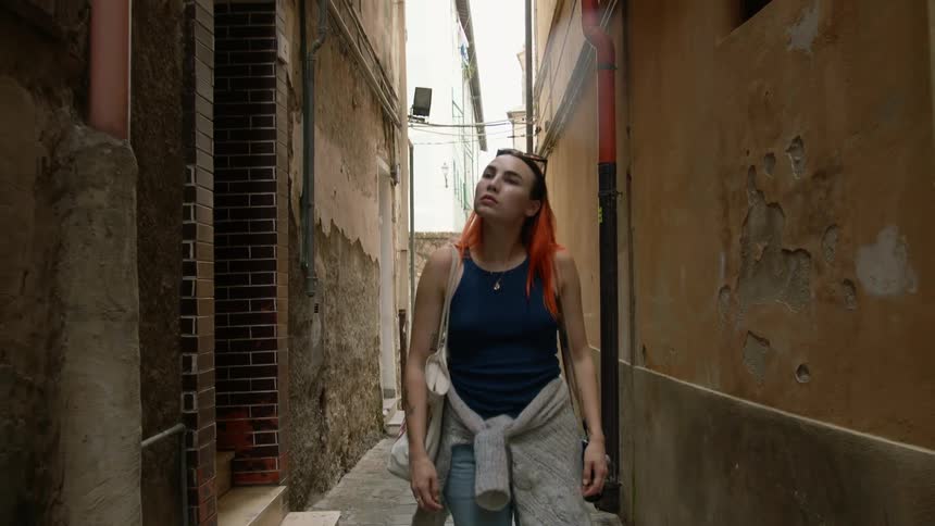 A woman looks all around her and she walks down an alley