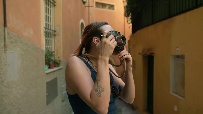 A woman in a tank top smiling while taking photos of buildings in a town