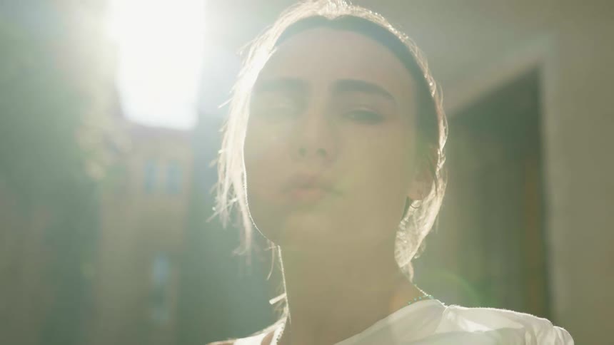 A portrait of a young woman outside near buildings on a sunny breezy day