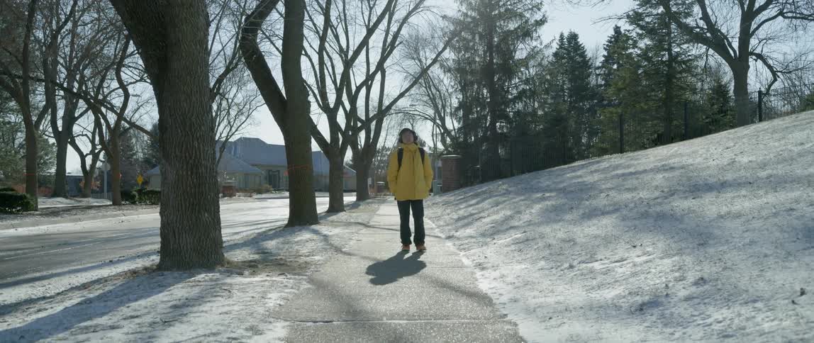 A boy in a yellow jacket walks down an icy sidewalk