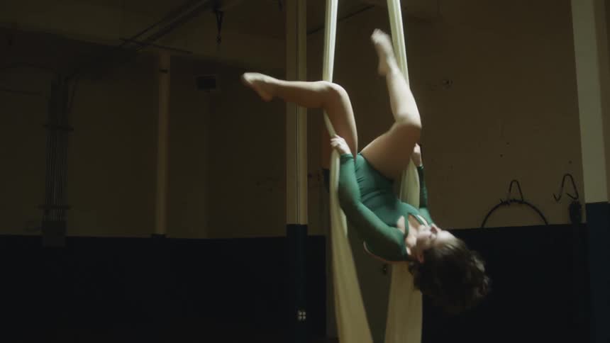 A female acrobat holds aerial silk and climbs up and spins around