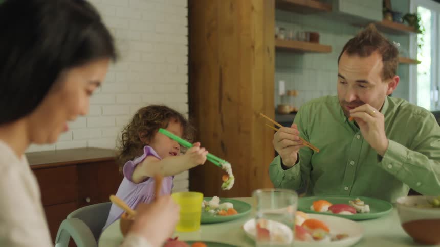 A young family eating sushi with chopsticks at home