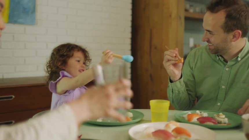 A small family is eating a meal as a child plays with her father at the dinner table