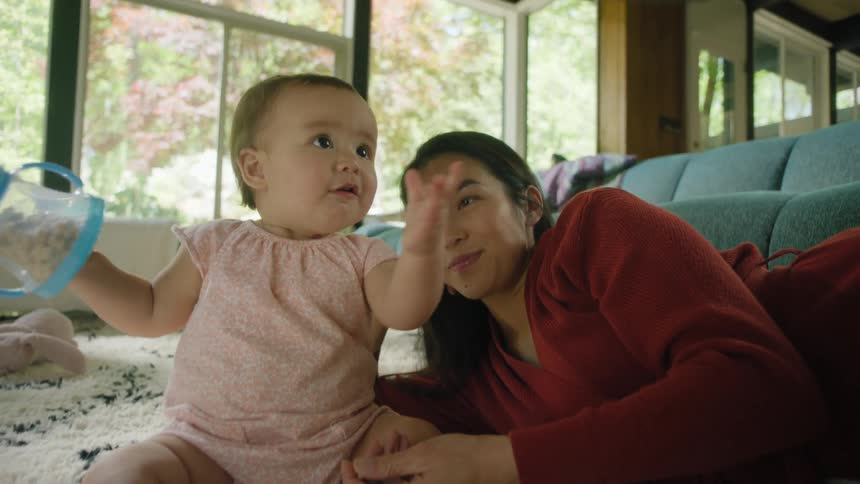 A woman and baby on the floor in a room with a couch and wall in the background