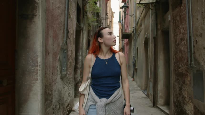 A woman looks at doorways and buildings as she walks down an alley in an old town