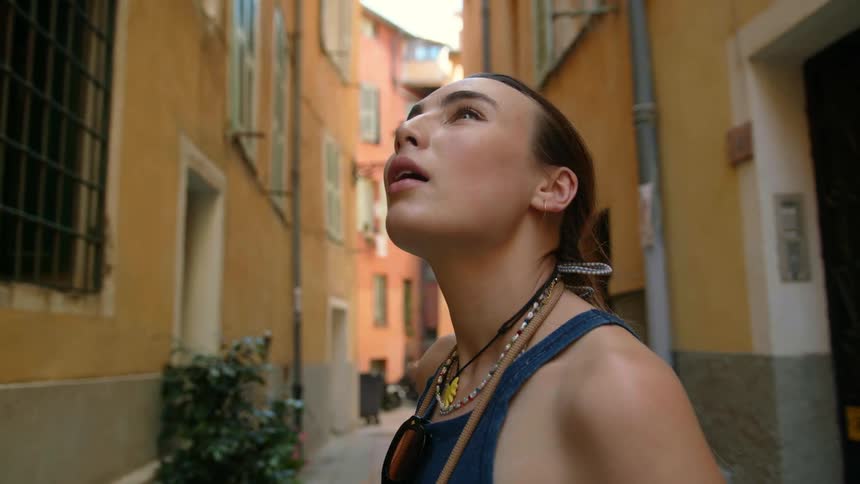 A woman looks up at buildings while standing in an alley