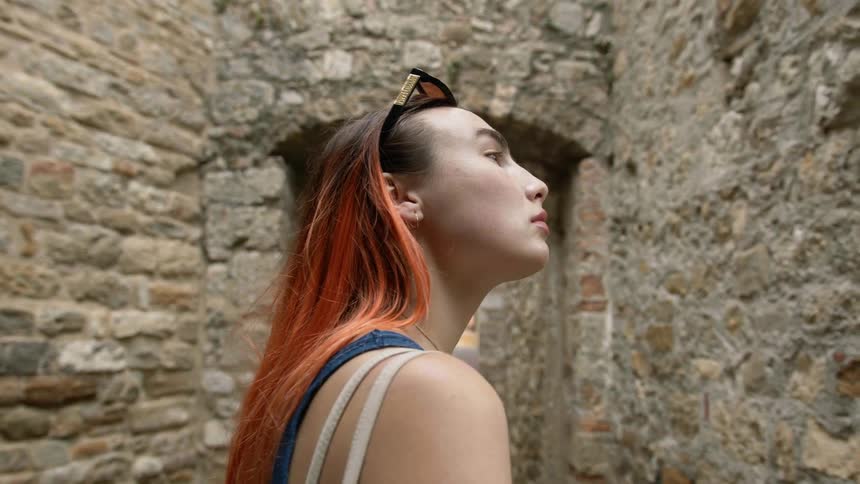 A woman with colorful dyed hair standing outside next to an old stone building