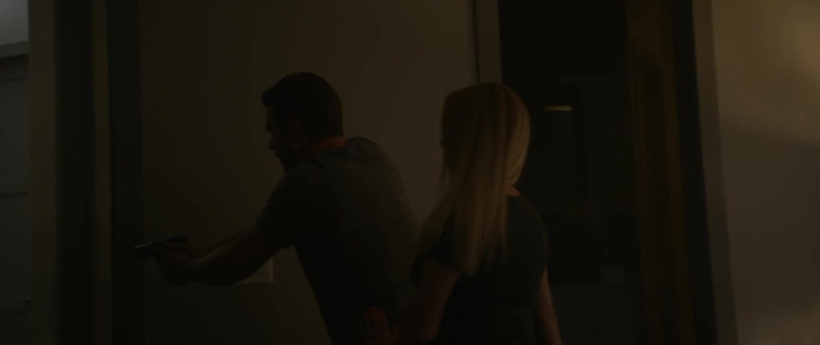 A man and women get out of bed and exit a dark bedroom